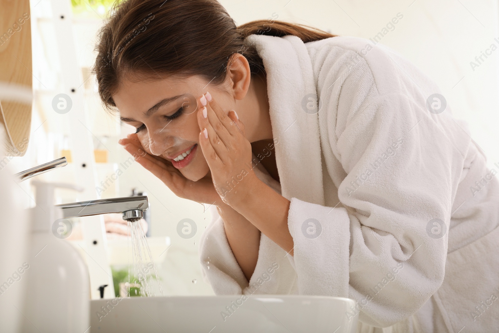 Photo of Beautiful teenage girl washing face with cleansing foam in bathroom. Skin care cosmetic