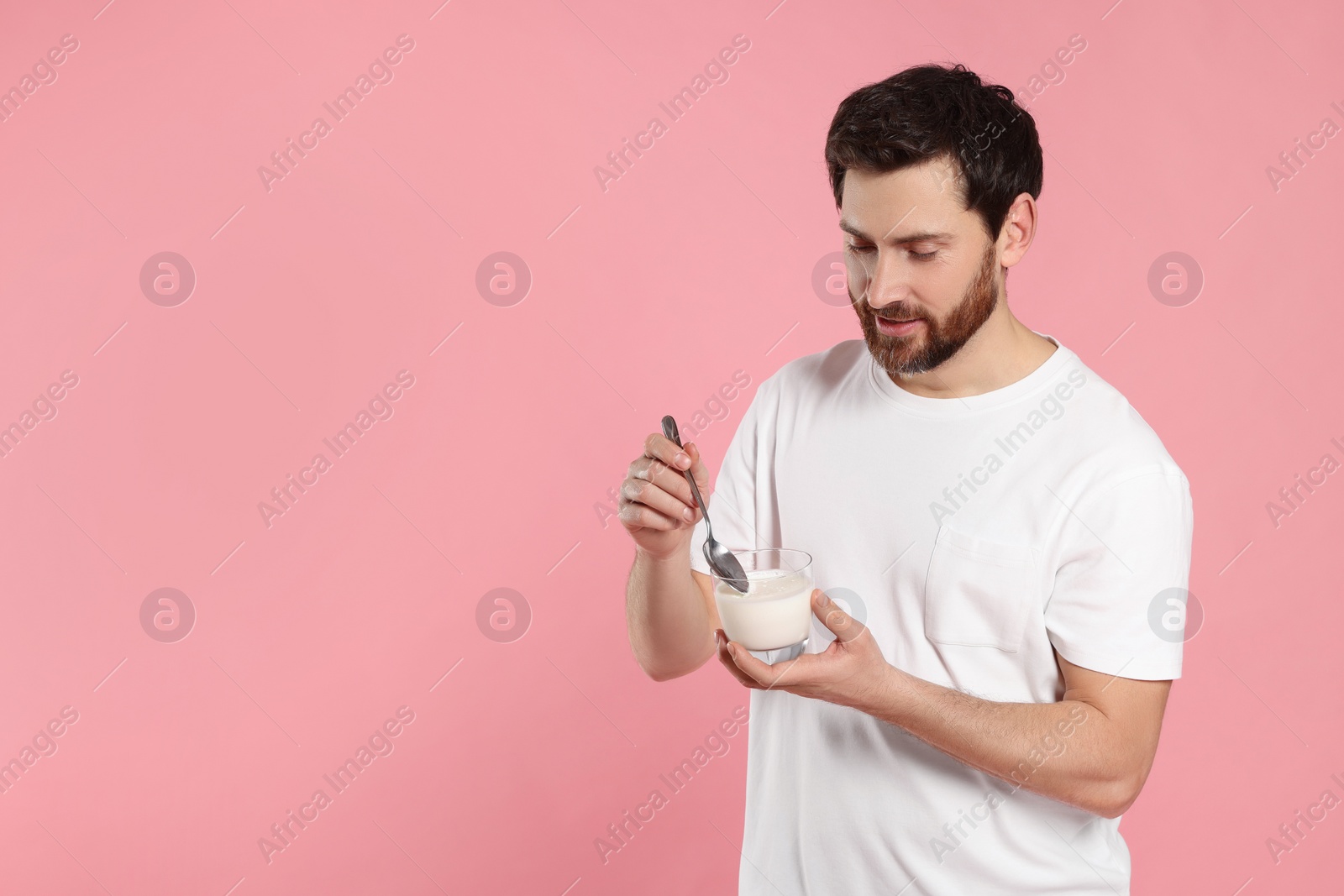 Photo of Handsome man with delicious yogurt and spoon on pink background. Space for text