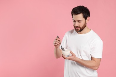 Handsome man with delicious yogurt and spoon on pink background. Space for text