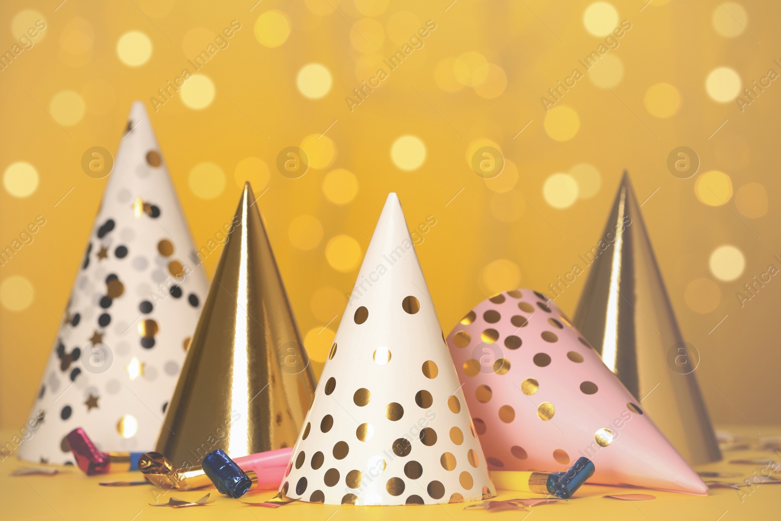 Photo of Party hats and festive items on table against yellow background with blurred lights