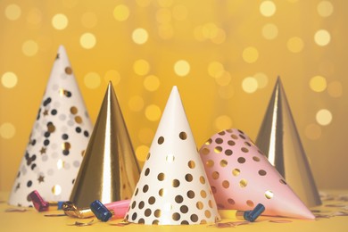 Photo of Party hats and festive items on table against yellow background with blurred lights