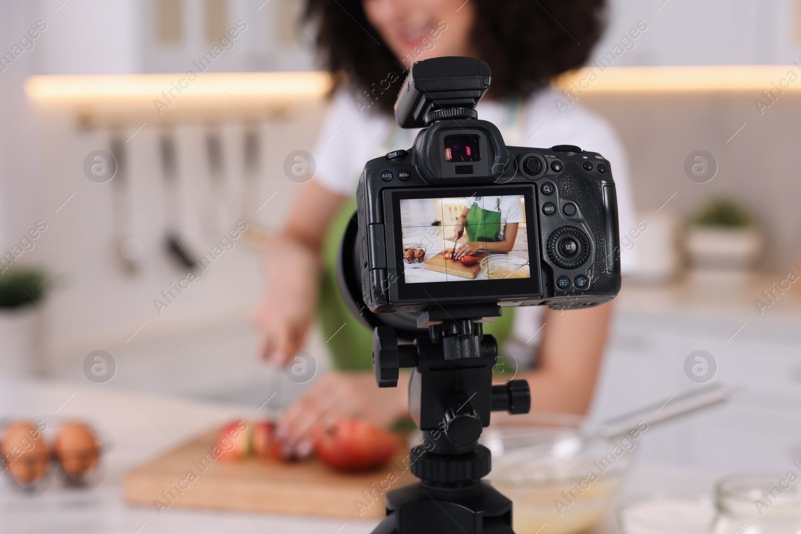 Photo of Food blogger cooking while recording video in kitchen, focus on camera