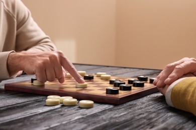 Photo of Man playing checkers with partner at black wooden table indoors, closeup