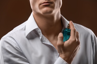 Photo of Handsome man in shirt using perfume on dark background, closeup