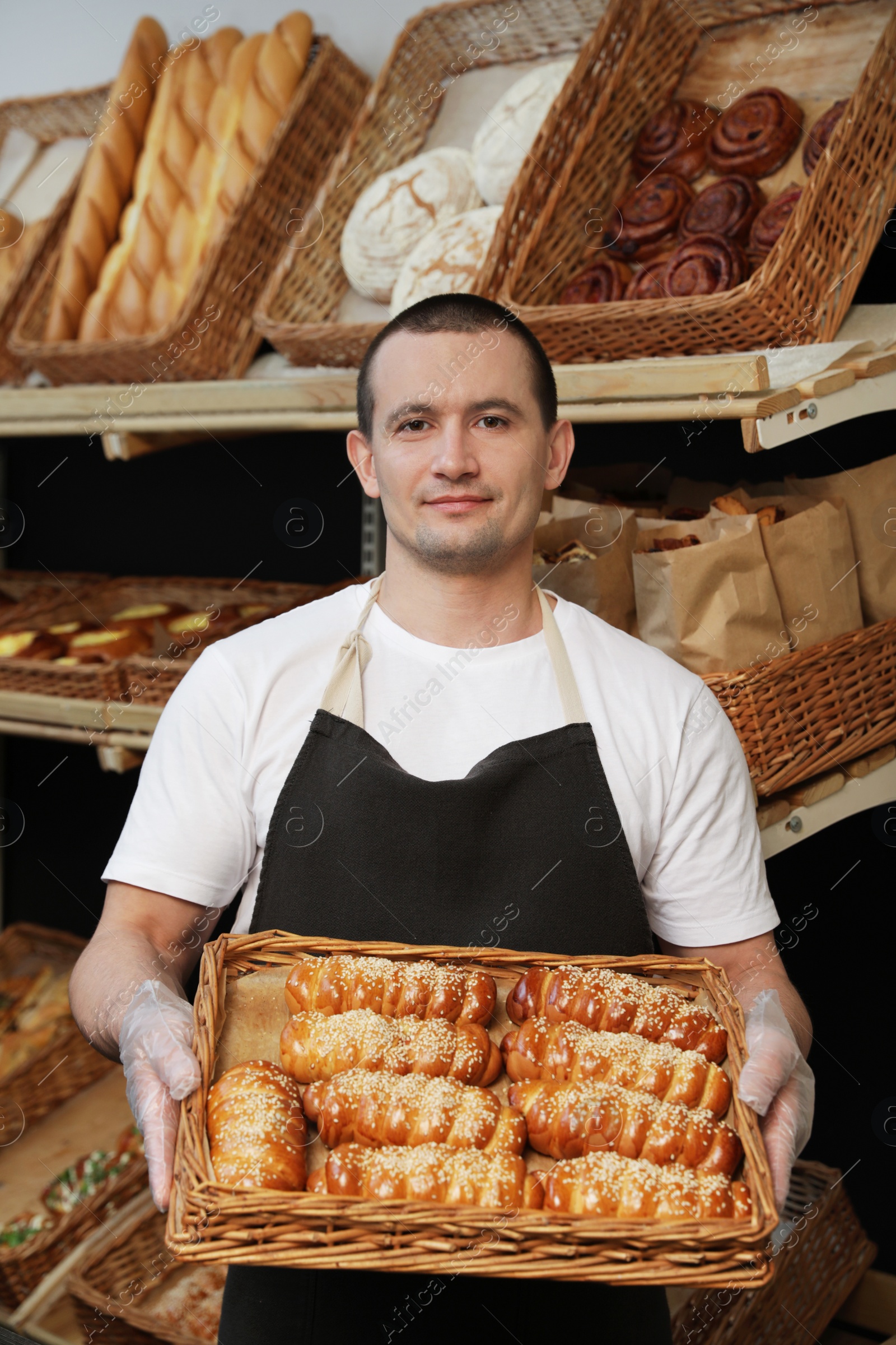 Photo of Portrait of professional baker holding tray with fresh buns near showcase in store