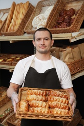 Portrait of professional baker holding tray with fresh buns near showcase in store