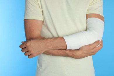 Man with arm wrapped in medical bandage on light blue background, closeup