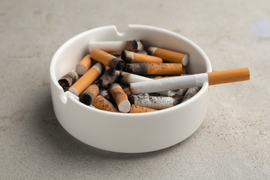 Photo of Ceramic ashtray full of cigarette stubs on grey table