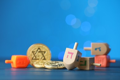 Photo of Hanukkah celebration. Dreidels with jewish letters and coins against blue background with blurred lights, closeup. Space for text