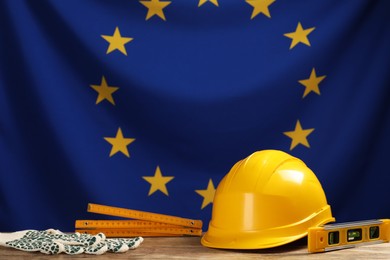 Photo of Different construction tools on wooden table against flag of European Union. Space for text