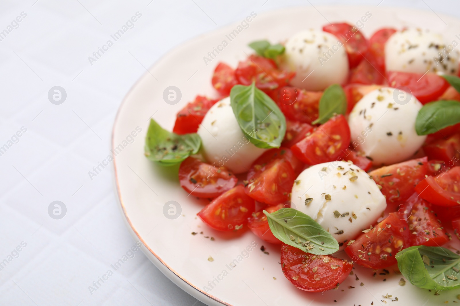 Photo of Tasty salad Caprese with tomatoes, mozzarella balls and basil on white tiled table, closeup. Space for text