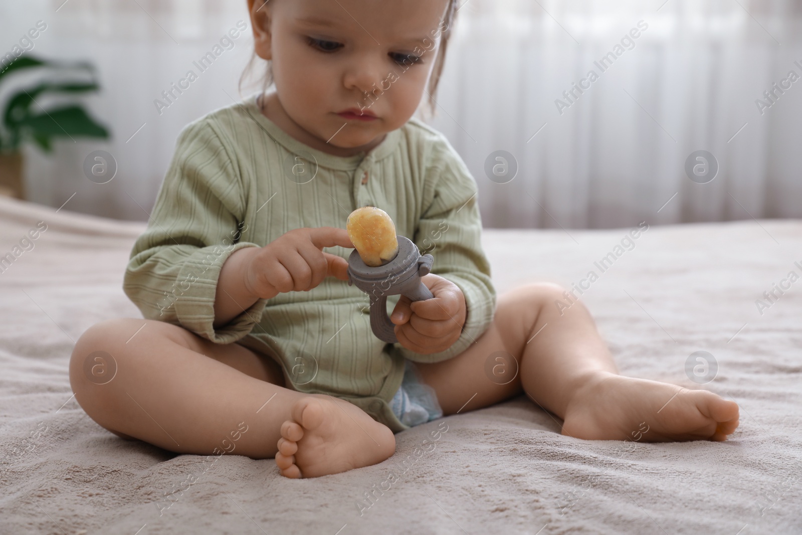 Photo of Cute baby girl with nibbler on bed at home