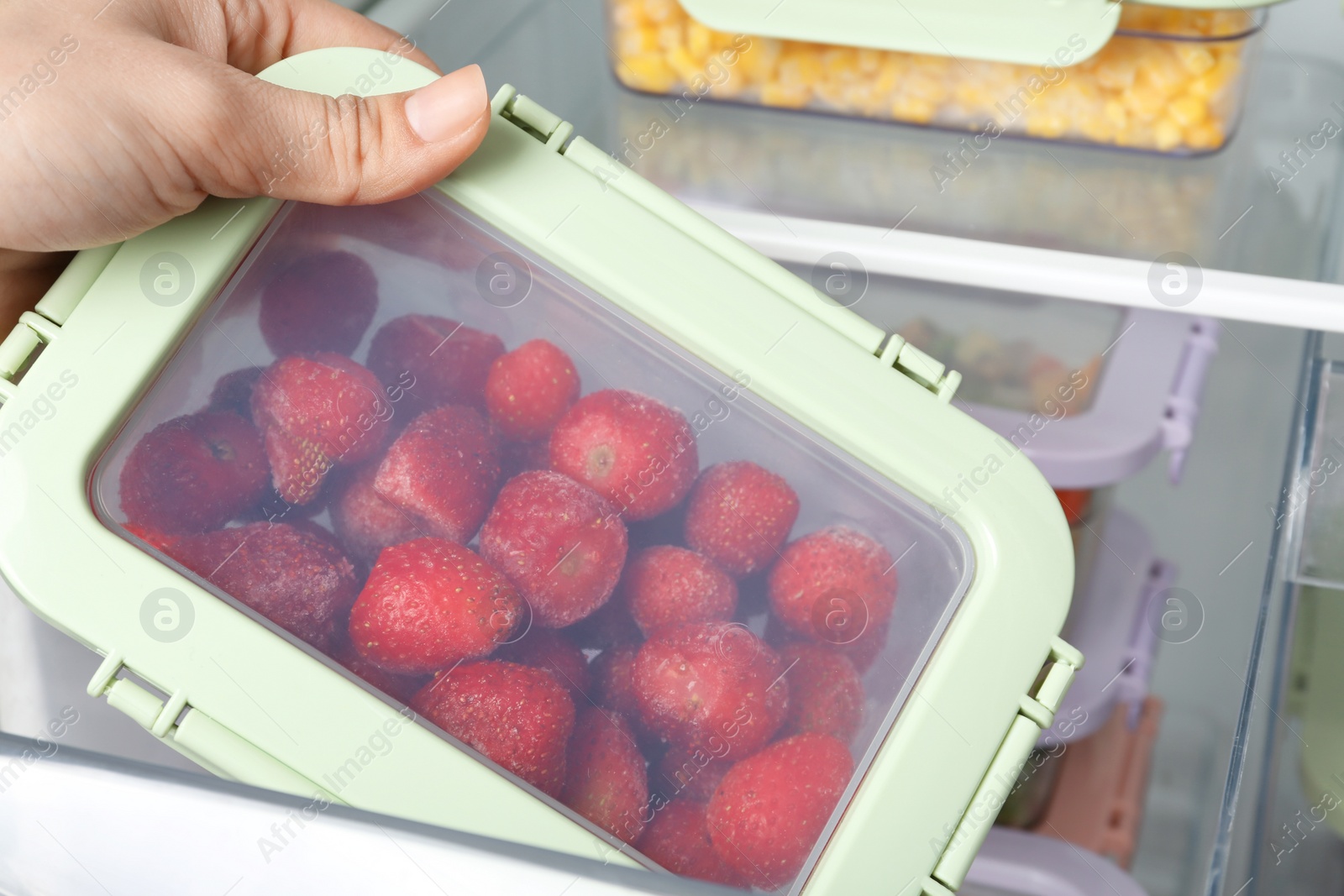 Photo of Woman taking box with frozen strawberry from refrigerator, closeup