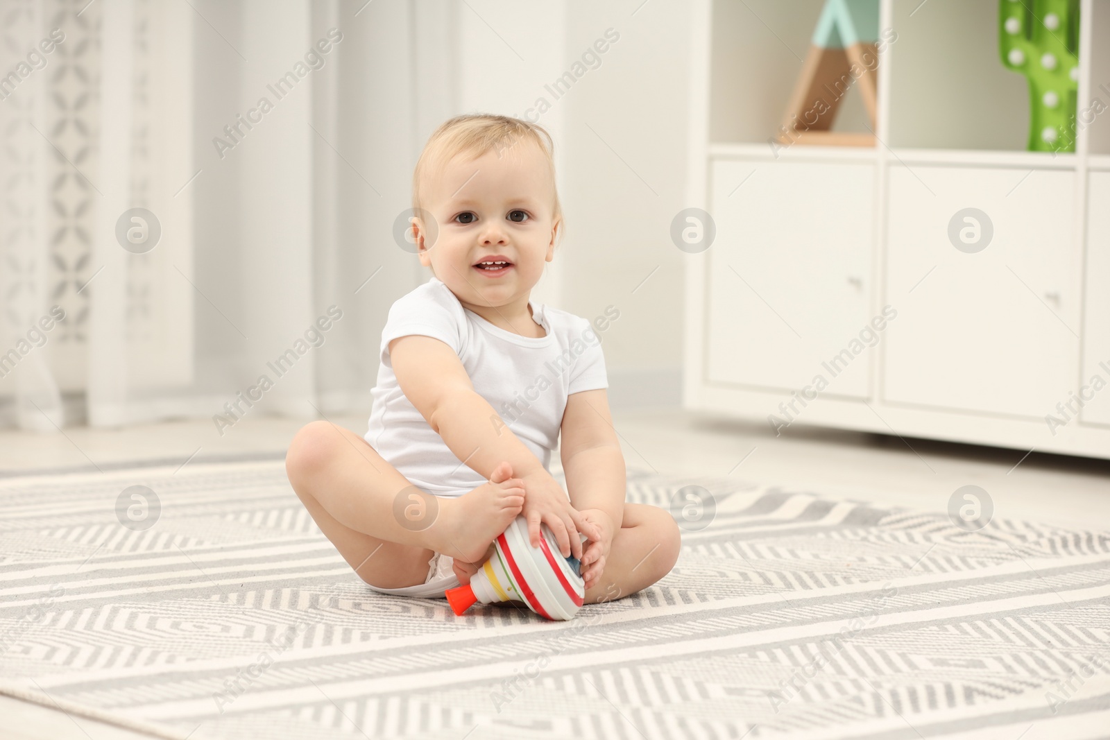 Photo of Children toys. Cute little boy playing with spinning top on rug at home