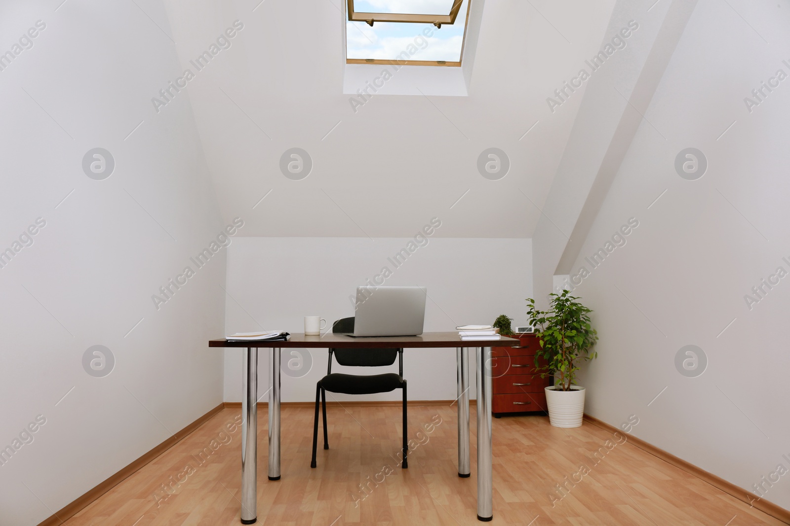 Photo of Stylish workplace with laptop and documents in attic room. Interior design