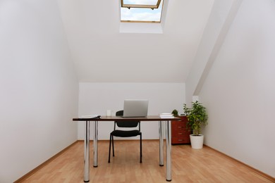 Photo of Stylish workplace with laptop and documents in attic room. Interior design