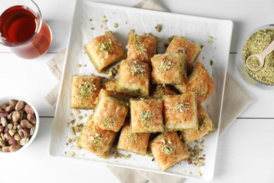 Photo of Delicious fresh baklava with chopped nuts served on white wooden table, flat lay. Eastern sweets