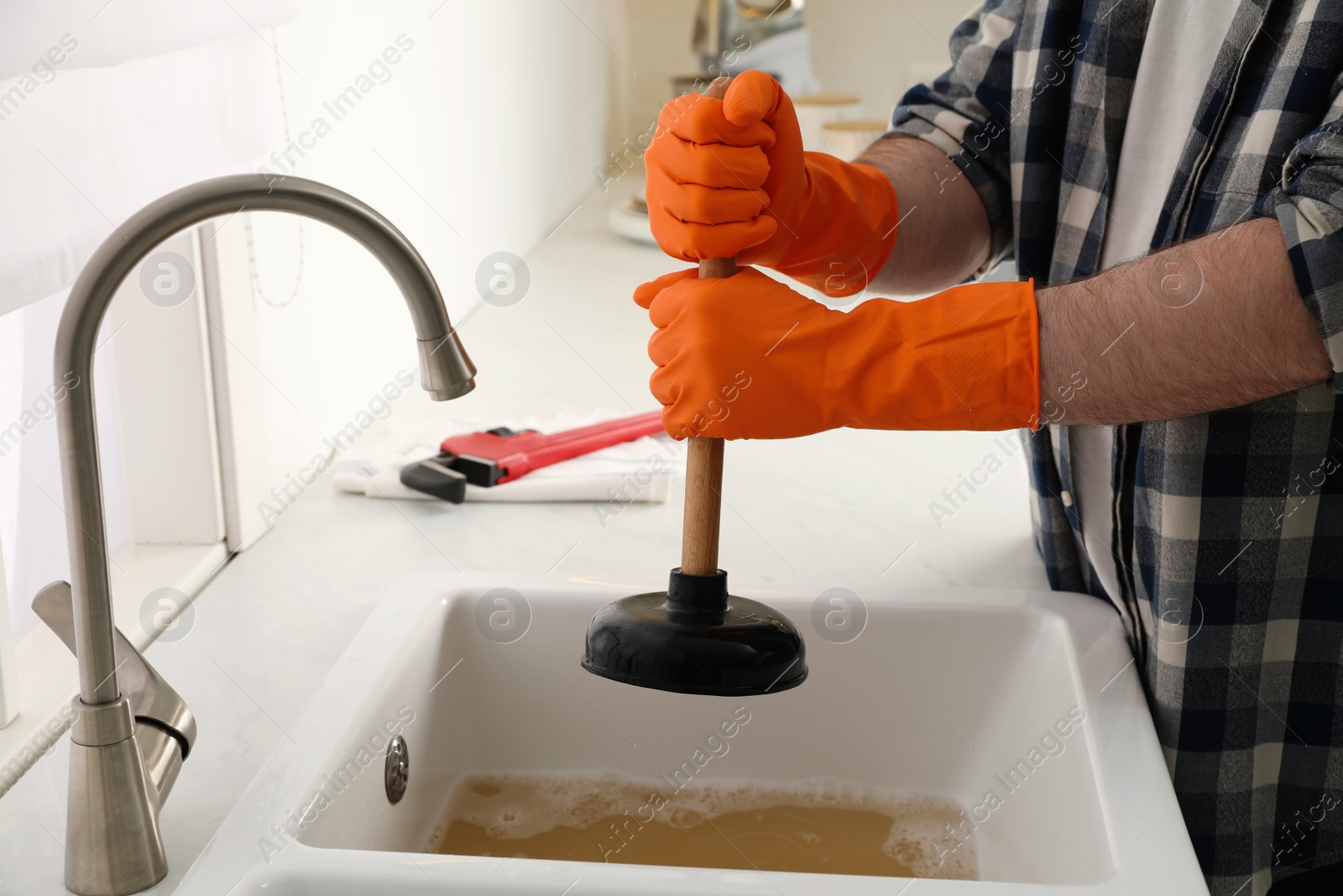 Photo of Man using plunger to unclog sink drain in kitchen, closeup