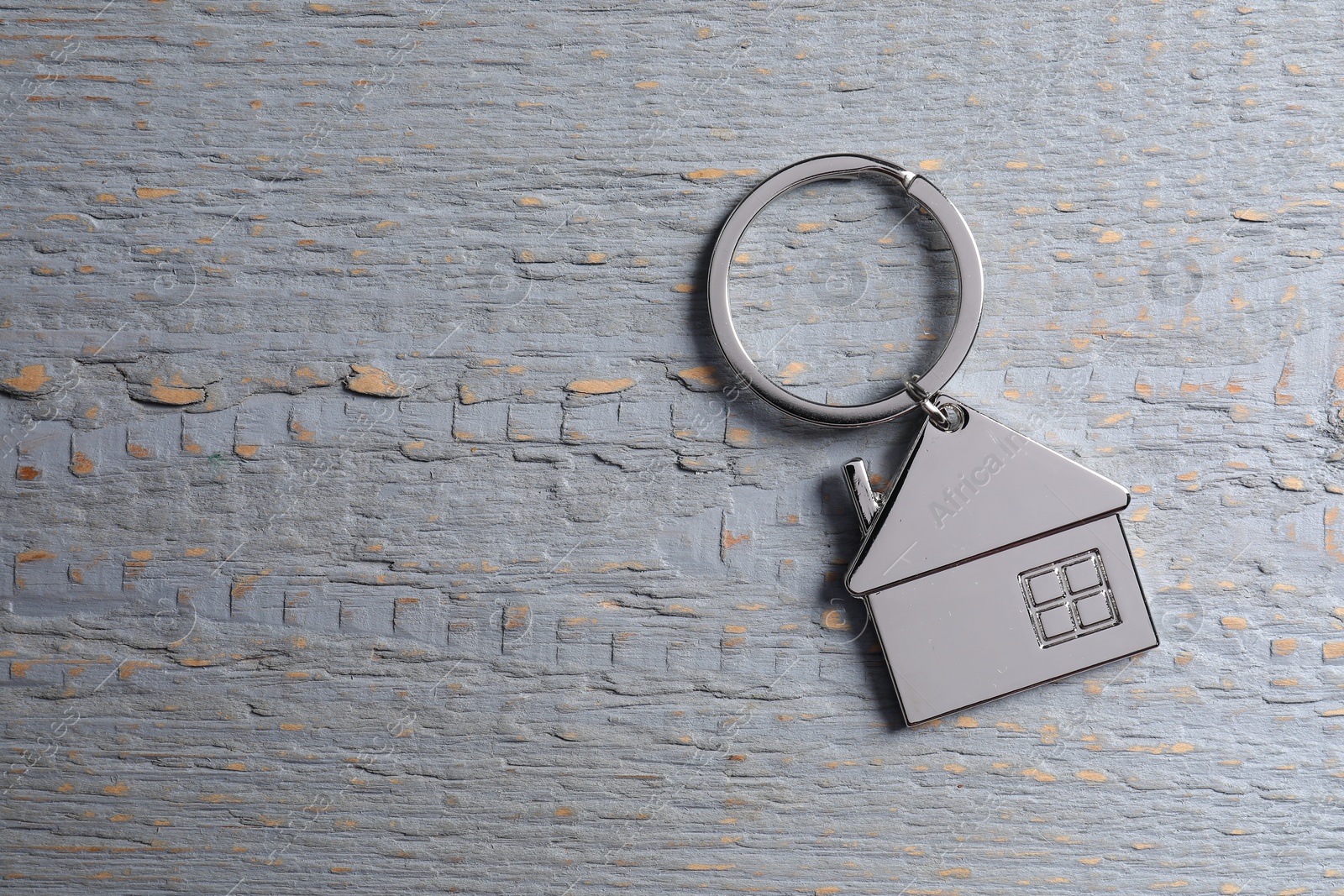 Photo of Metal keychain in shape of house on grey wooden table, top view. Space for text