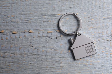 Photo of Metal keychain in shape of house on grey wooden table, top view. Space for text