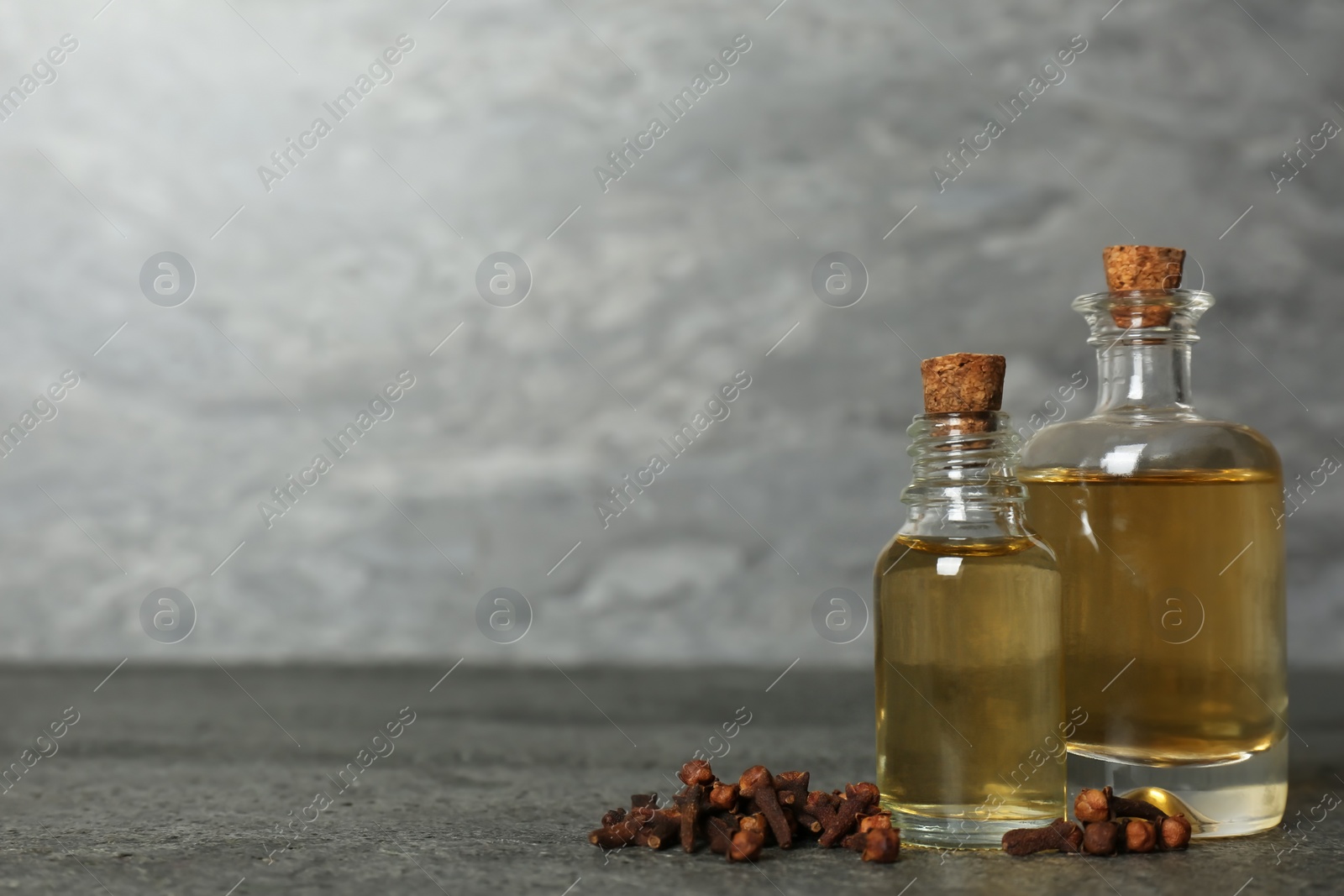 Photo of Essential oil and dried cloves on grey table. Space for text