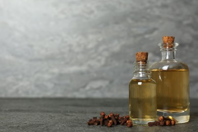 Essential oil and dried cloves on grey table. Space for text