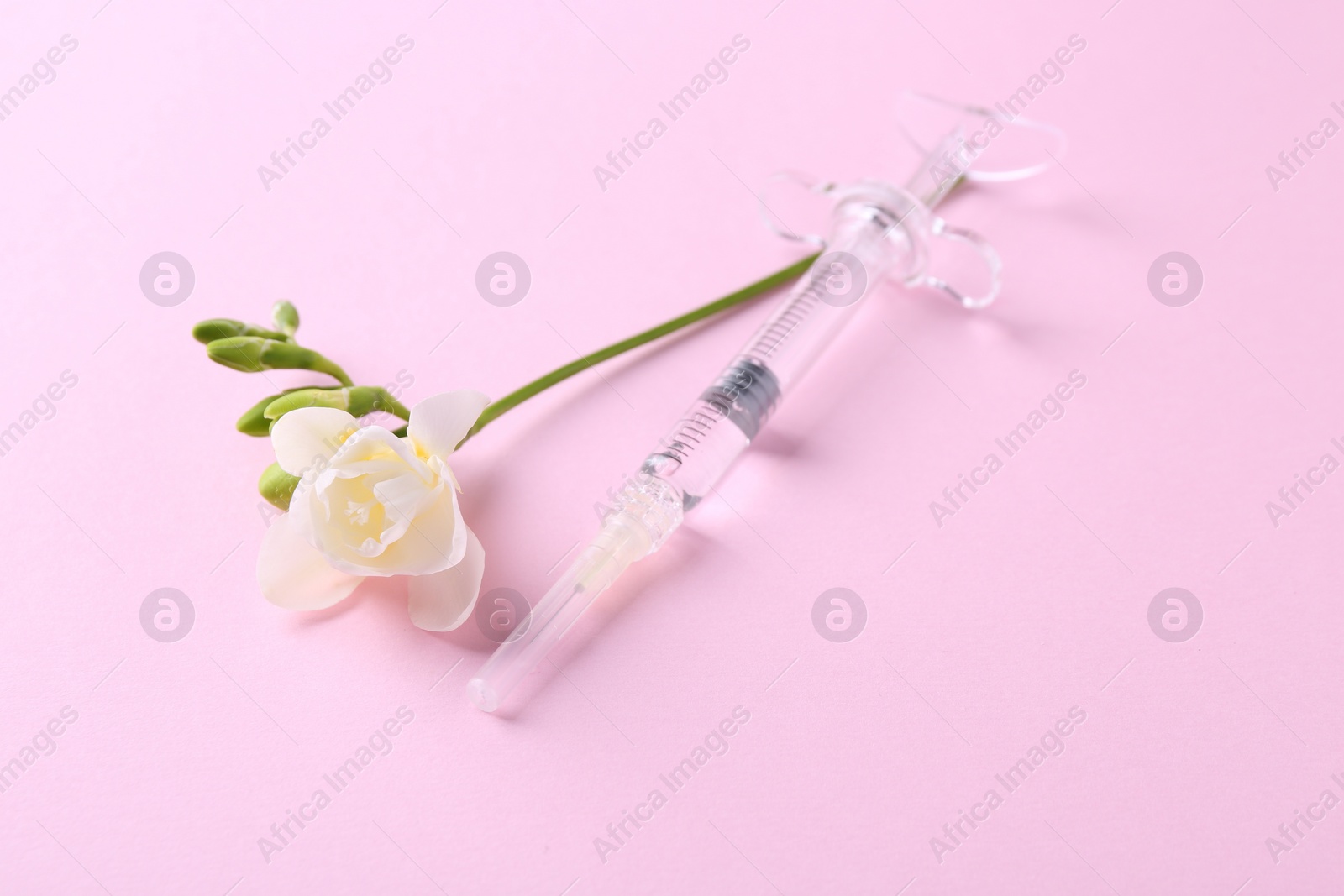 Photo of Cosmetology. Medical syringe and freesia flower on pink background, closeup