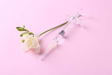 Cosmetology. Medical syringe and freesia flower on pink background, closeup