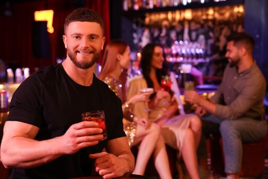 Photo of Friends spending time together in bar. Handsome man with fresh alcoholic cocktail, space for text