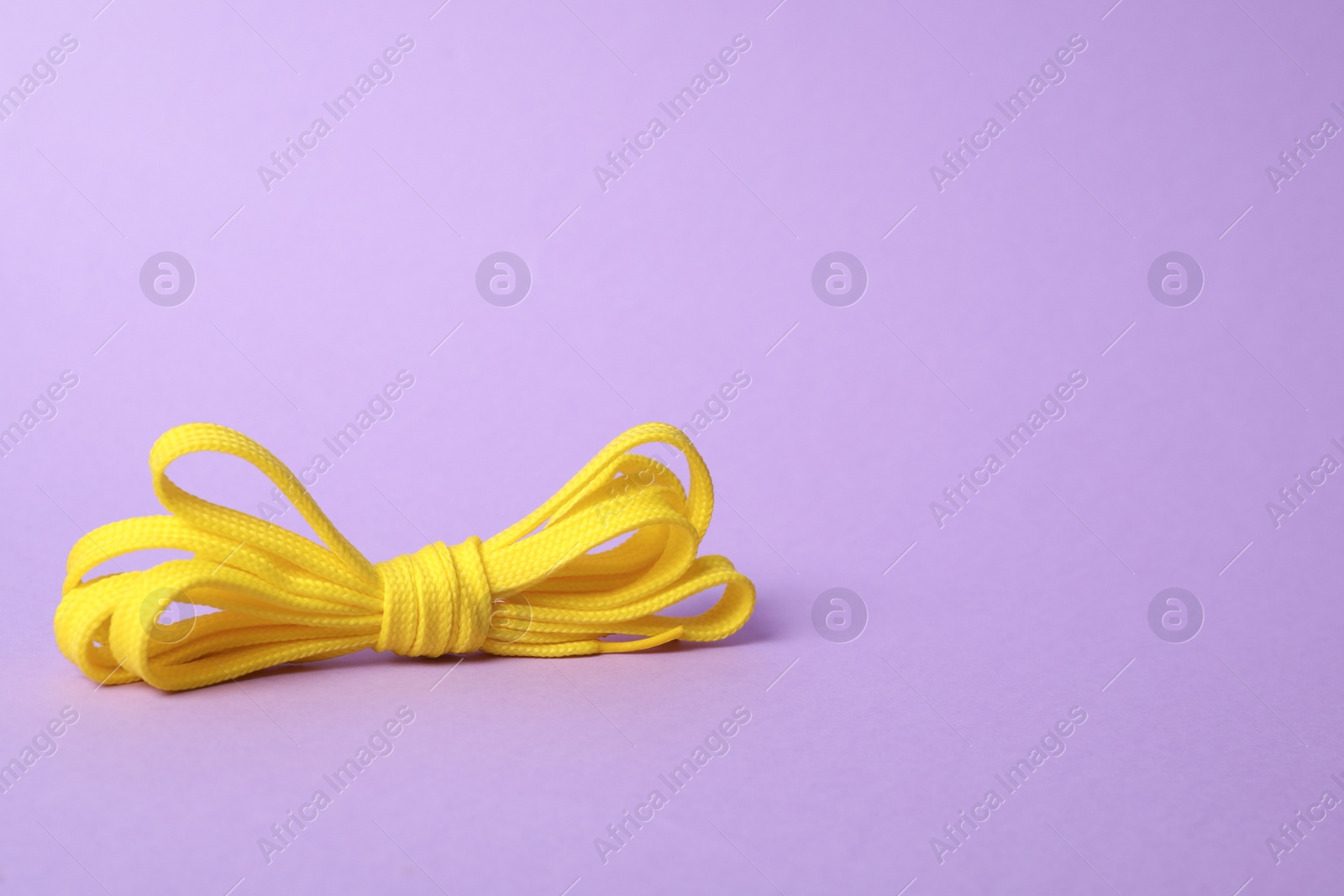 Photo of Yellow shoe lace tied in bow on lilac background. Space for text