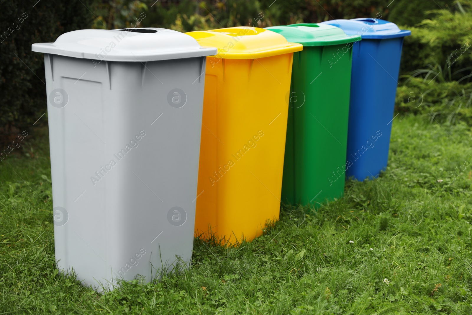 Photo of Many color recycling bins on green grass outdoors