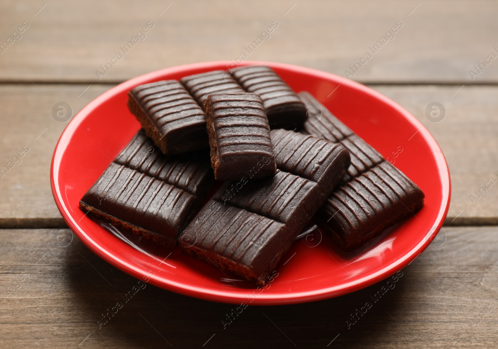 Photo of Red plate with delicious and healthy hematogen on wooden table, closeup