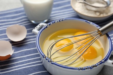 Photo of Whisk and eggs in pot on table, closeup