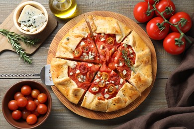 Flat lay composition of tasty galette with tomato, rosemary and cheese (Caprese galette) on wooden table