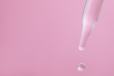 Dripping serum from pipette on pink background, closeup. Space for text