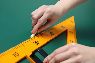 Photo of Woman drawing with chalk and triangle ruler on green board, closeup
