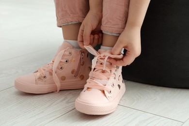 Photo of Little girl tying shoe laces at home, closeup