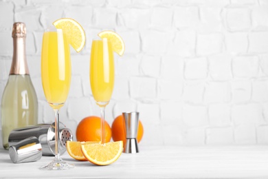 Fresh alcoholic Mimosa cocktails and fresh orange fruits on white wooden table, space for text