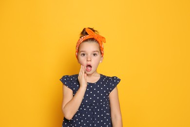 Photo of Emotional little girl wearing stylish bandana on orange background