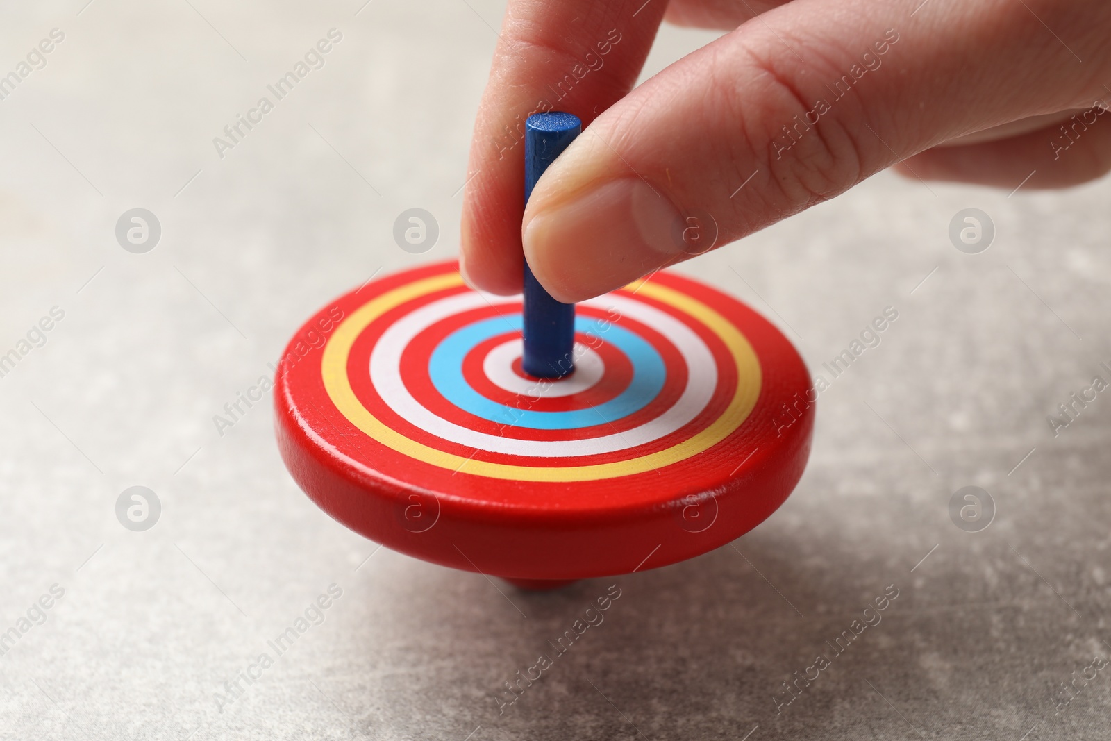 Photo of Woman playing with bright spinning top at grey textured background, closeup