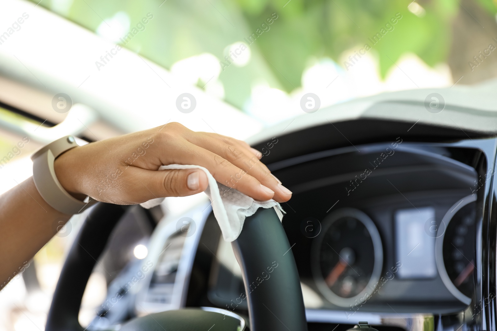 Photo of Woman cleaning steering wheel with wet wipe in car, closeup. Coronavirus pandemic