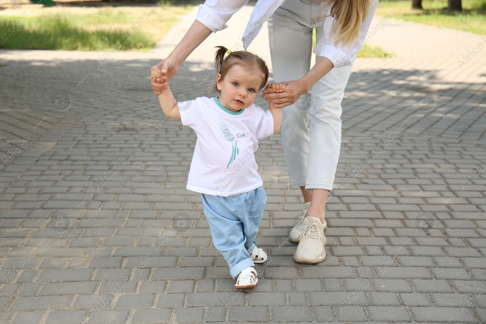 Photo of Mother supporting daughter while she learning to walk outdoors, closeup