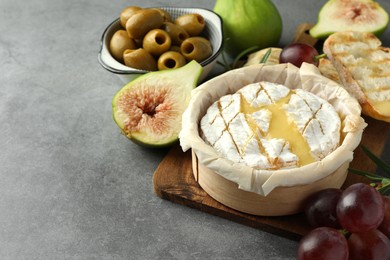 Photo of Tasty baked brie cheese and products on grey table. Space for text