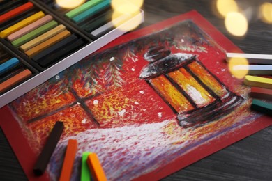 Photo of Colorful chalk pastels and beautiful painting on black wooden table. Bokeh effect