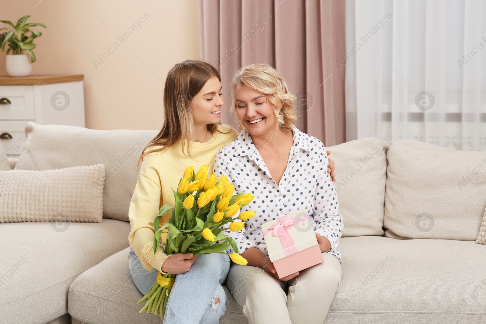 Photo of Young daughter congratulating her mom with flowers and gift at home. Happy Mother's Day