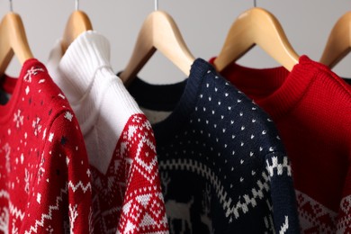 Different Christmas sweaters hanging on rack against light background, closeup