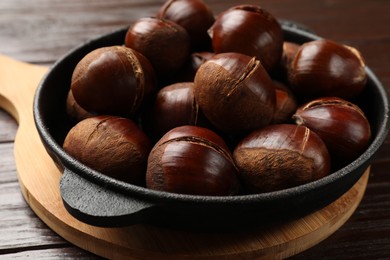 Photo of Roasted edible sweet chestnuts in baking dish on wooden table, closeup