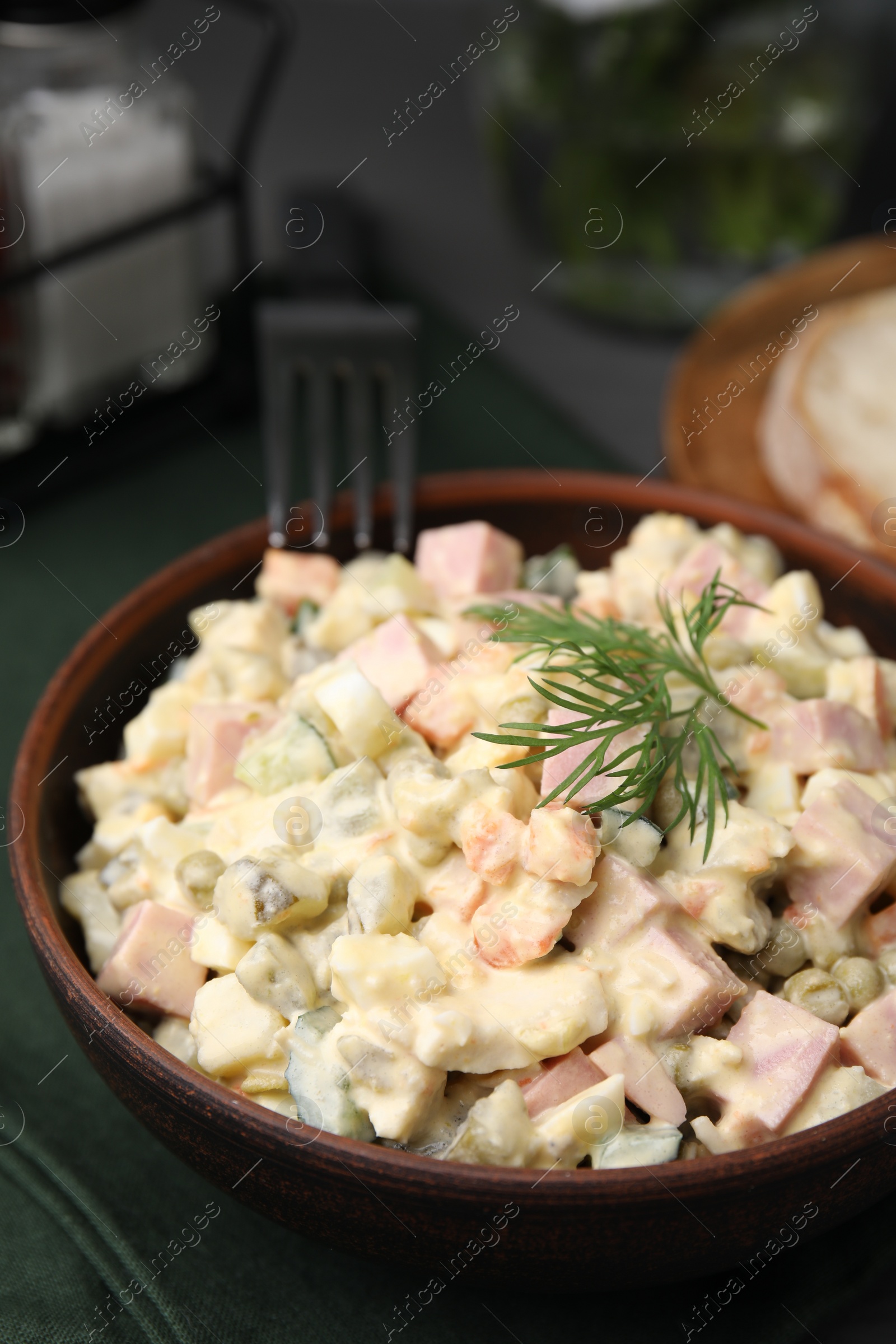 Photo of Tasty Olivier salad with boiled sausage in bowl on table, closeup