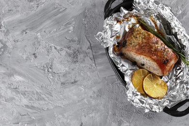 Photo of Tasty pork baked in foil and lemon slices on grey textured table, top view. Space for text