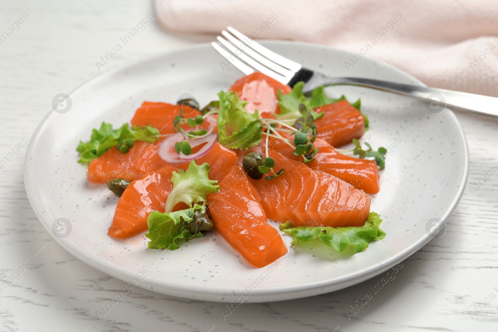 Photo of Salmon carpaccio with capers, lettuce, microgreens and onion on white wooden table, closeup